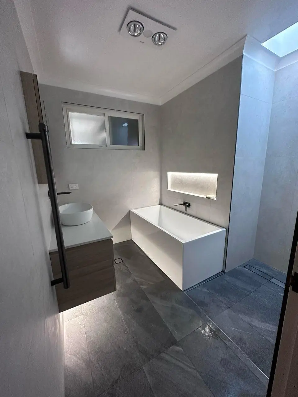 Renovated Newcastle bathroom with a back to wall bath, wall hung vanity, heated towel rail and a walk-in shower under a skylight