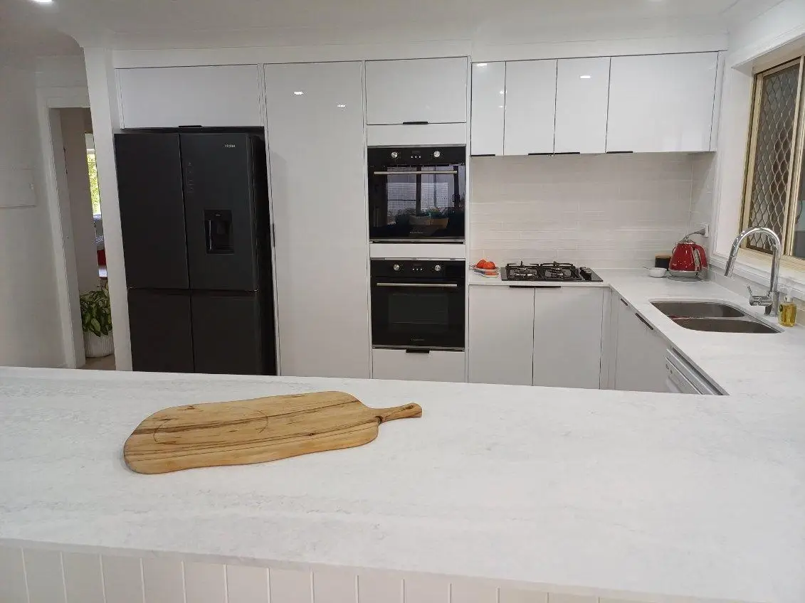 Kitchen viewed across the peninsula, showing overhead cupboards, tiled splashback, wall ovens and a gas cooktop